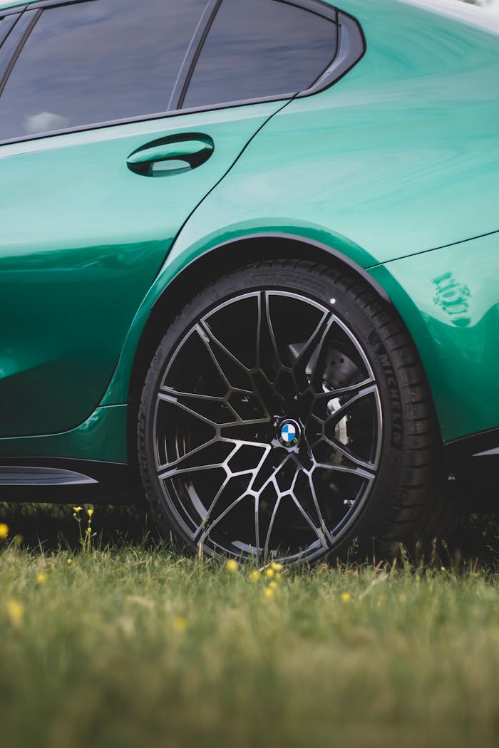 why-choose-us A close-up of a green BMW M3 featuring elegant black alloy wheels parked outdoors on the grass.